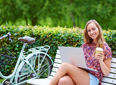 Buy stock photo Shot of a young woman using a laptop on a bench while out for a cycle in the park