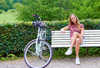 Buy stock photo Shot of a young woman sitting on a bench while out for a cycle in the park