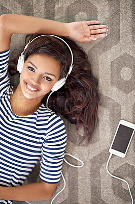 Buy stock photo High angle portrait of a young woman listening to music on her cellphone while lying on the floor
