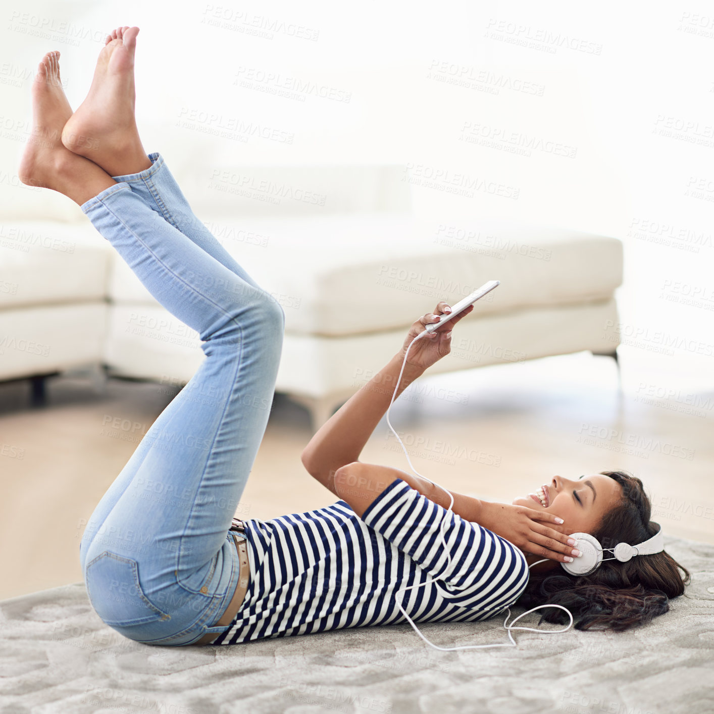 Buy stock photo Shot of a young woman listening to music on her cellphone while lying on the floor