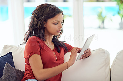 Buy stock photo Cropped shot of a young woman using her tablet while relaxing at home