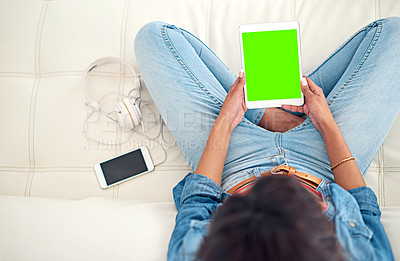 Buy stock photo High angle shot of a young woman using her digital tablet while sitting on the sofa