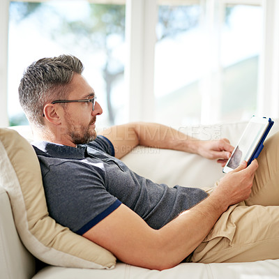 Buy stock photo Man, relax and tablet on living room sofa, reading and social media for video, game or movies in home. Mature guy, digital touchscreen and lounge couch for internet blog, news and web app in house