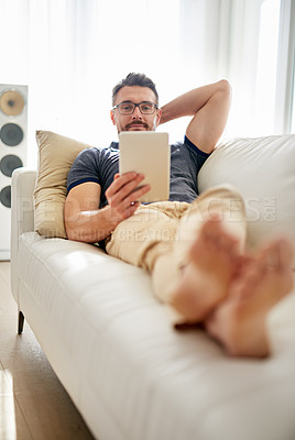 Buy stock photo Shot of a man using his tablet while relaxing on the sofa at home