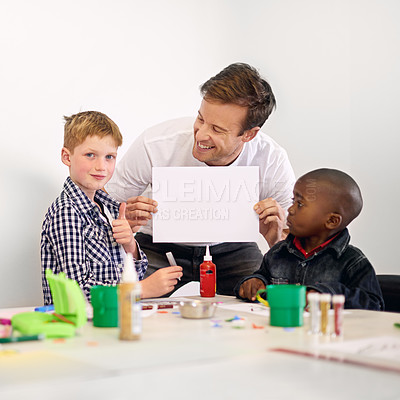 Buy stock photo Shot of a volunteer holding up a blank sign while working with little children