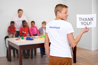 Buy stock photo Shot of a volunteer holding a 'volunteers needed' sign  with volunteers working with little children in the background