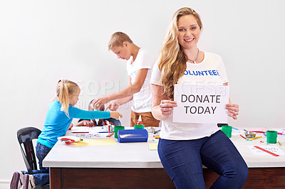 Buy stock photo Portrait of a volunteer holding up a 'donate today' sign while working with little children