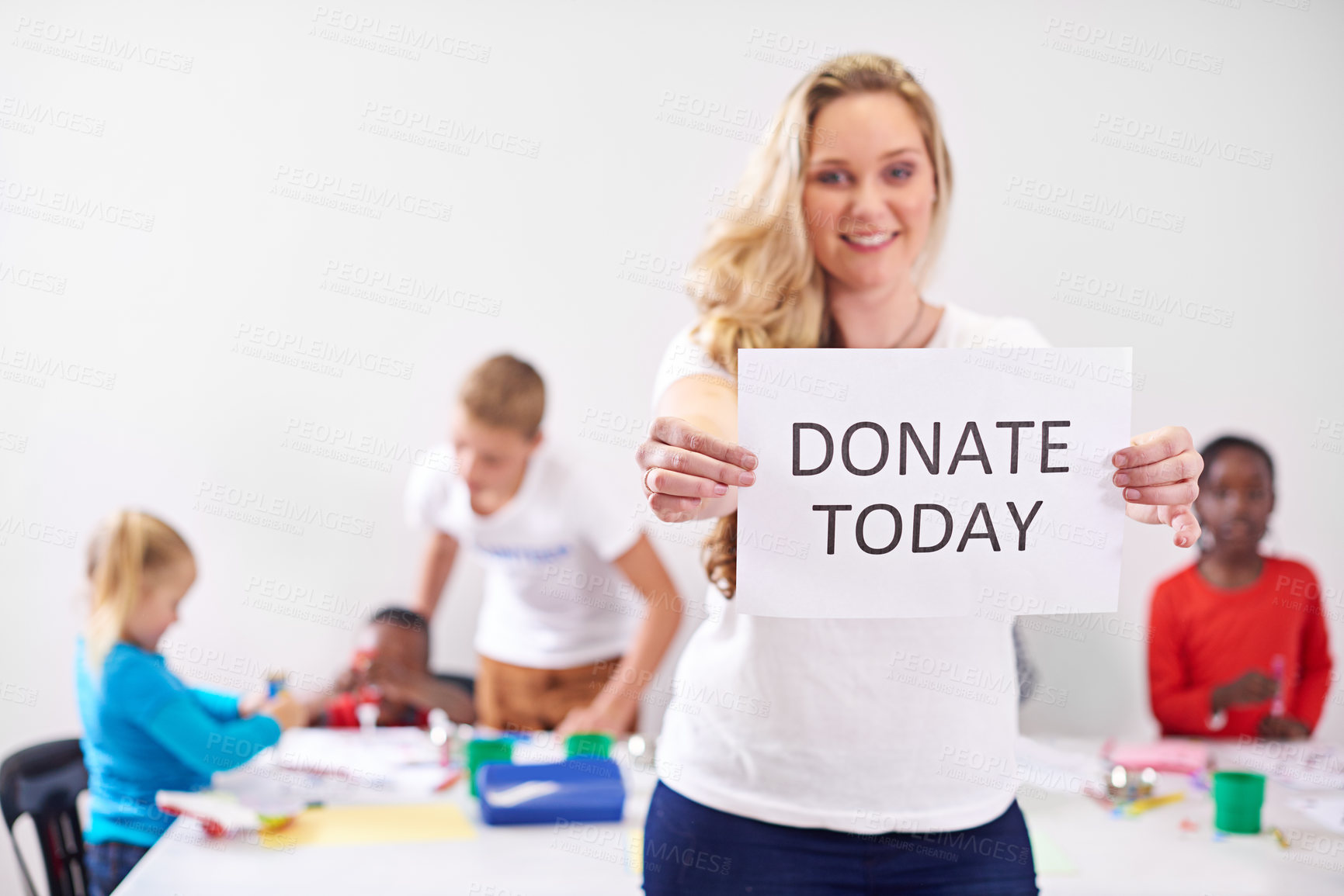 Buy stock photo Portrait of a volunteer holding up a 'donate today' sign while working with little children