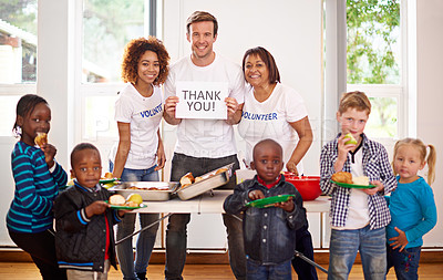 Buy stock photo Portrait of a volunteer holding up a 'thank you' sign while feeding little children