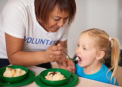 Buy stock photo Shot of a volunteer feeding a little girl at a youth center