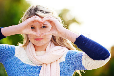 Buy stock photo Cropped portrait of a young woman looking through her hands while making a heart shape outdoors