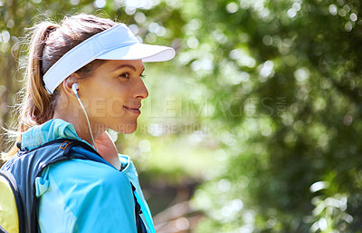Buy stock photo Shot of woman listening to music on earphones while out for a trail run
