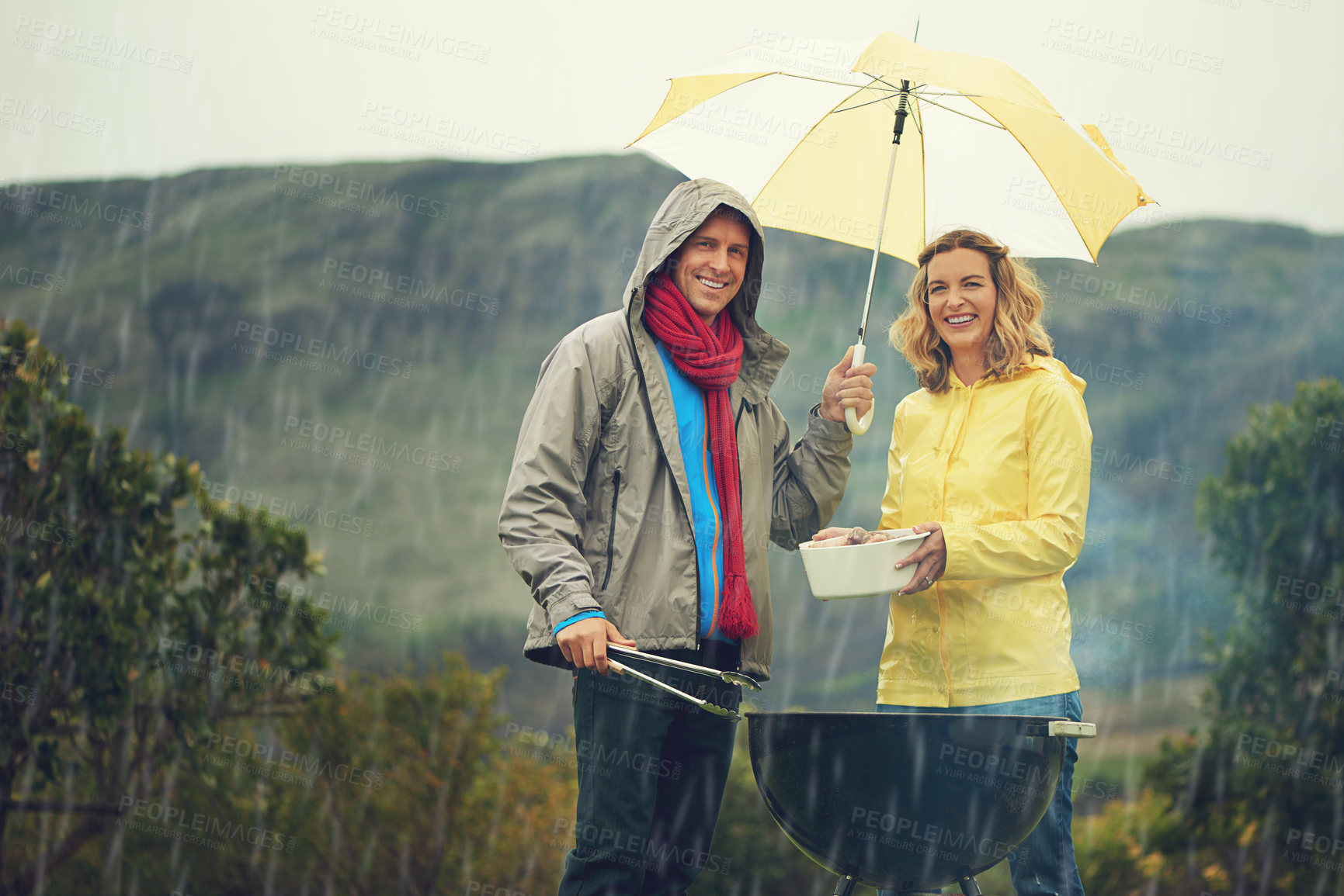 Buy stock photo Shot of a couple happily barbecuing in the rain