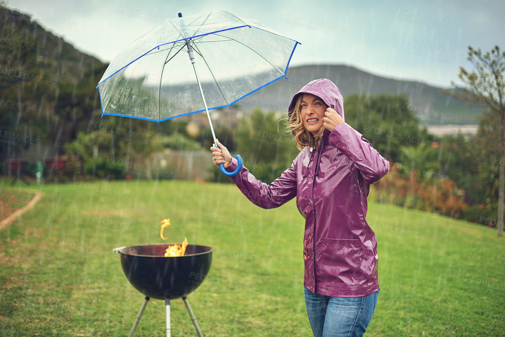 Buy stock photo Shot of a woman holiding an umbrella while trying to barbeque in the rain