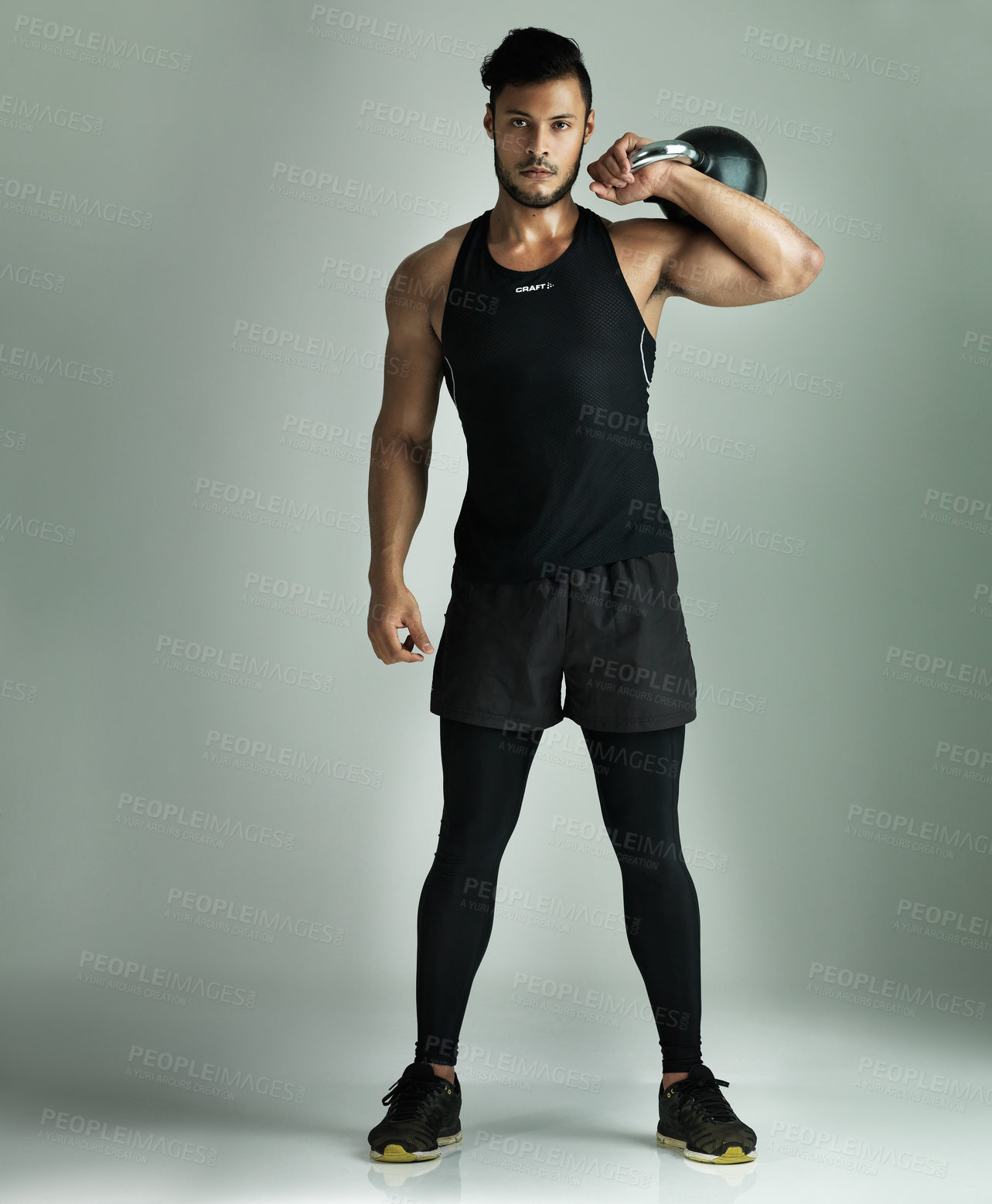 Buy stock photo Studio shot of a young man working out with a kettle bell against a gray background