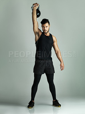 Buy stock photo Studio shot of a young man working out with a kettle bell against a gray background