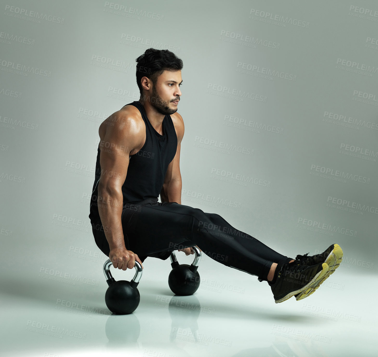 Buy stock photo Studio shot of a young man working out with kettle bells against a gray background