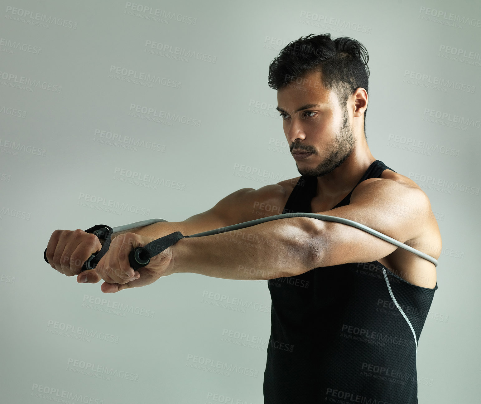 Buy stock photo Studio shot of a young man working out with a resistance band against a gray background