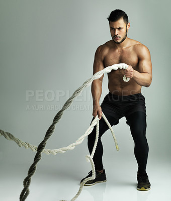 Buy stock photo Studio shot of a young man working out with a heavy rope against a gray background