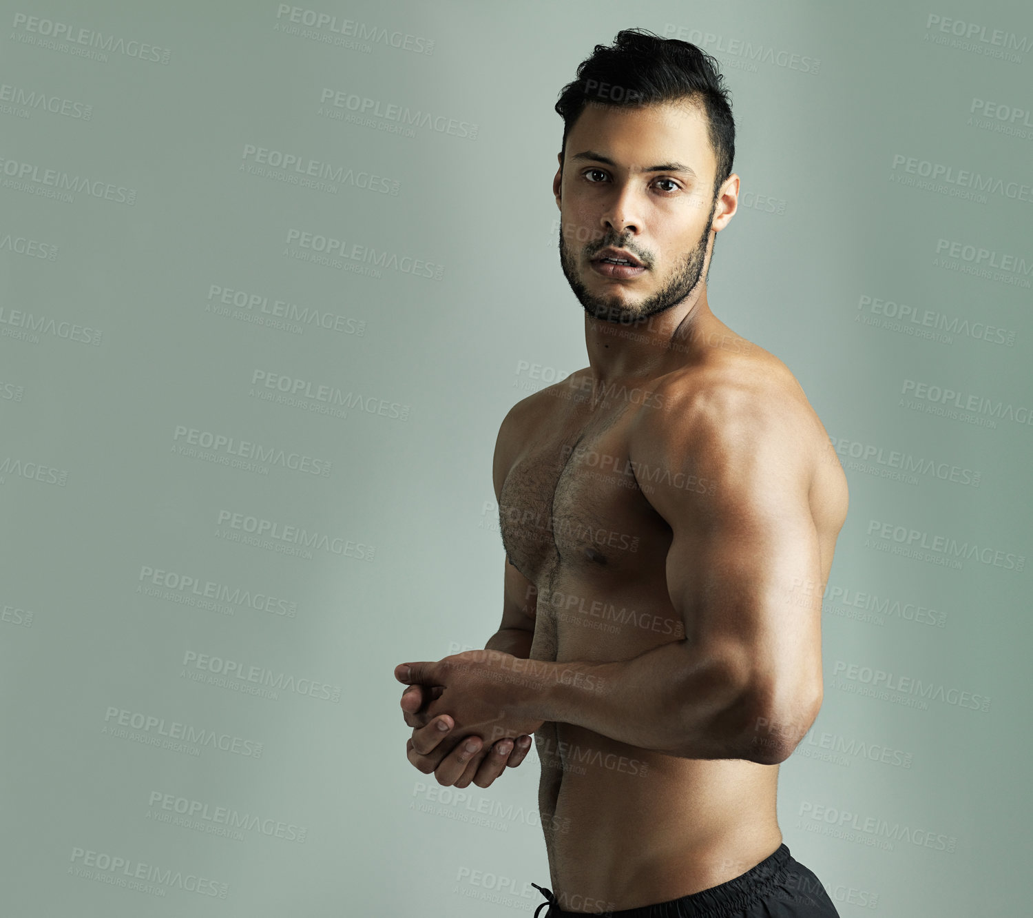 Buy stock photo Studio shot of an athletic young man flexing his muscles against a gray background