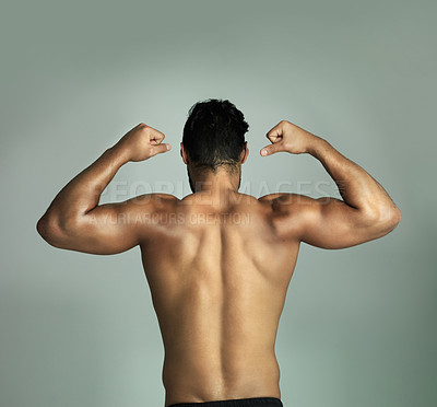 Buy stock photo Rearview shot of an athletic young man flexing his muscles against a gray background