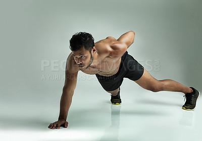Buy stock photo Studio shot of a young man doing a one hand pushup against a gray background