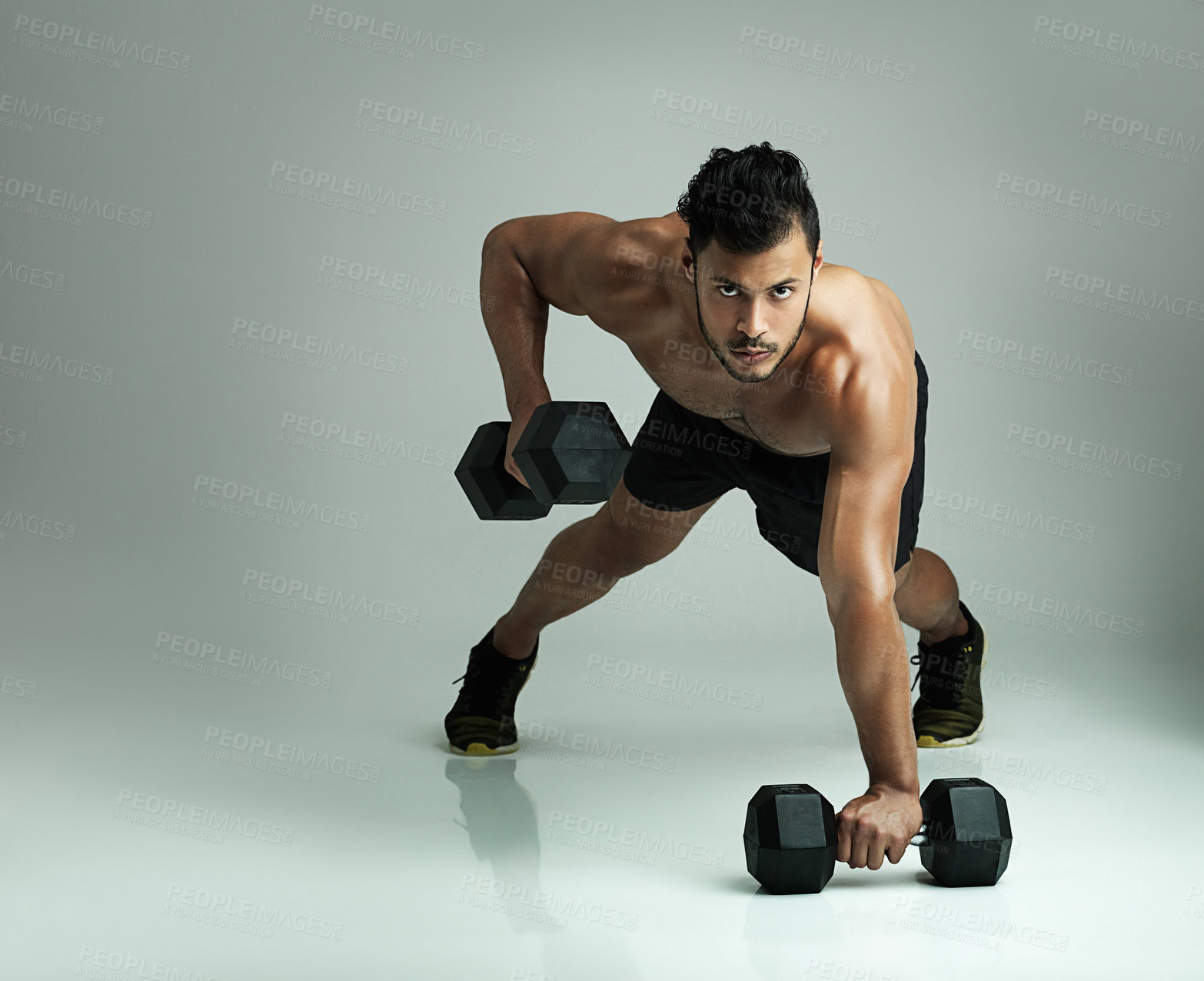 Buy stock photo Studio shot of a young man working out with dumbbells against a gray background