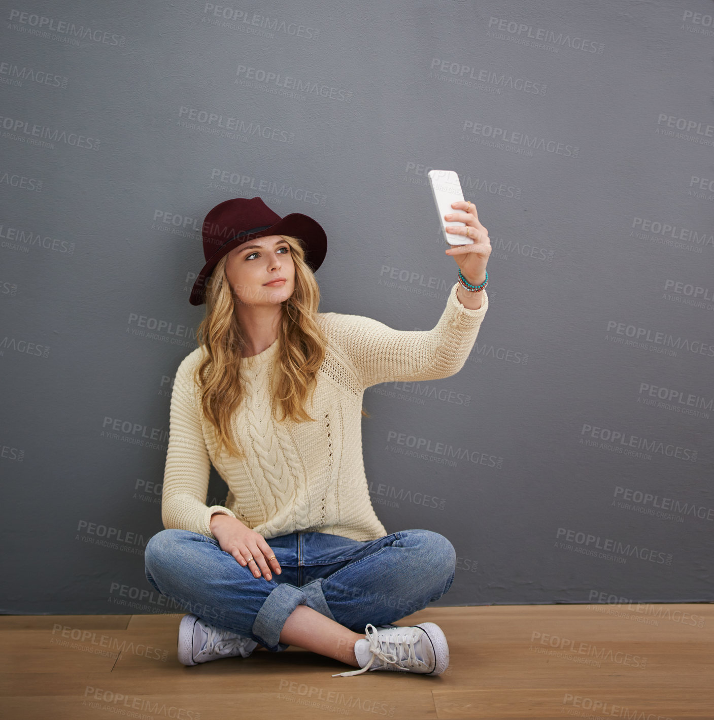 Buy stock photo Shot of a young woman using her cellphone while sitting against a gray background