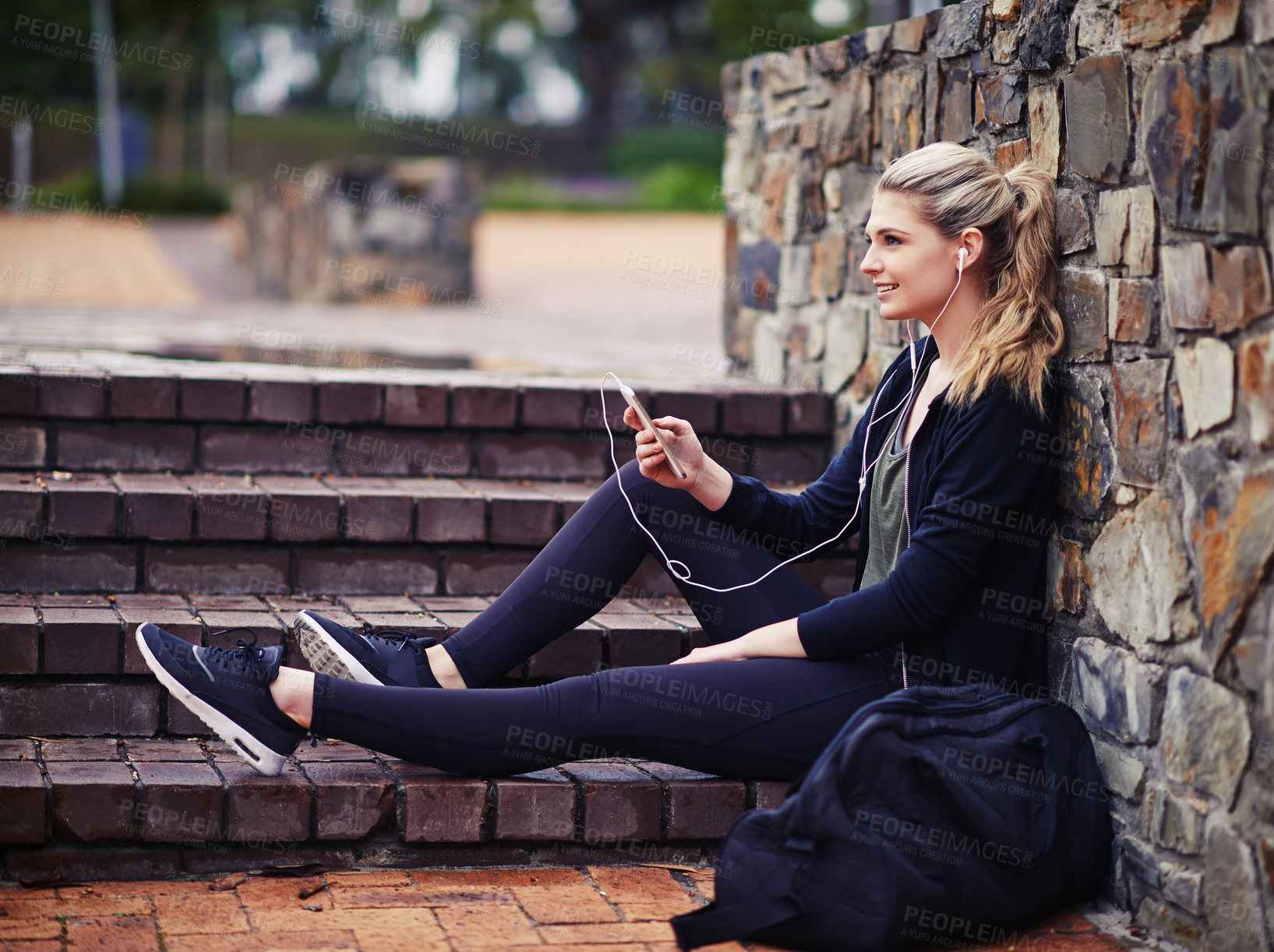 Buy stock photo Shot of a sporty young woman listening to music while sitting outside