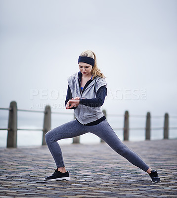 Buy stock photo Shot of a young woman checking her watch while exercising outdoors