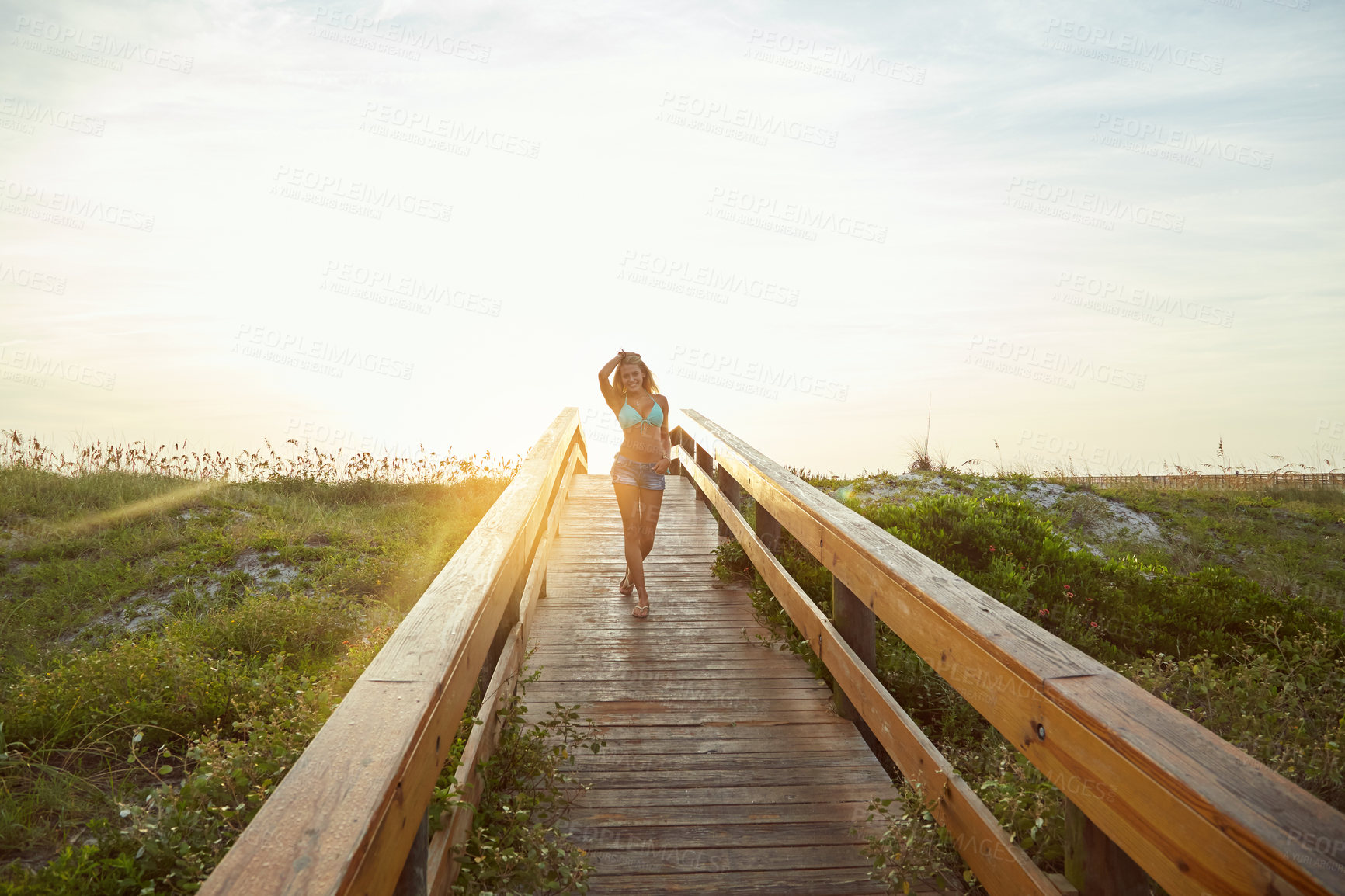 Buy stock photo Shot of a young woman in a bikini on a walkway near the beach