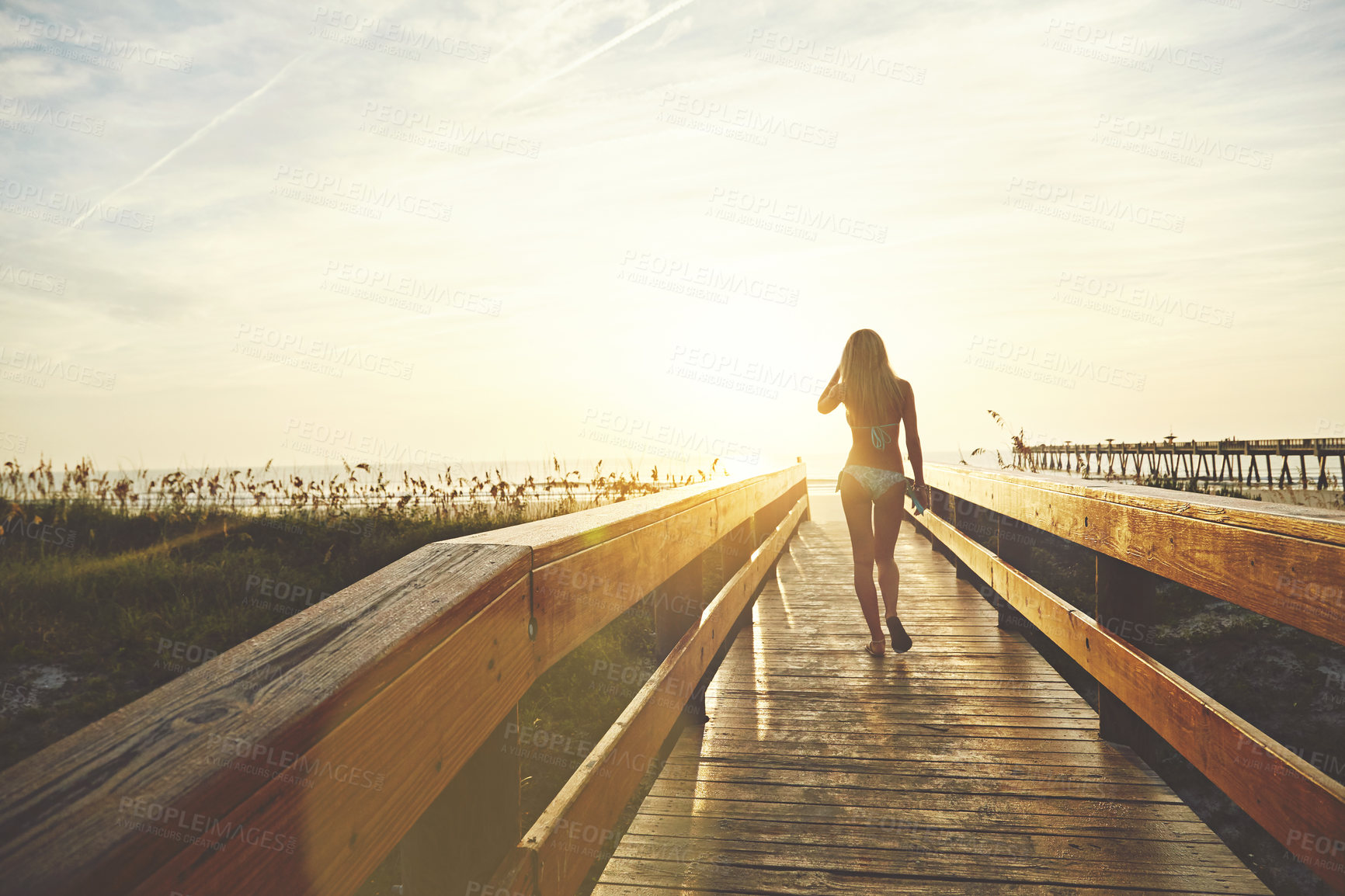 Buy stock photo Shot of a young woman in a bikini on a walkway near the beach