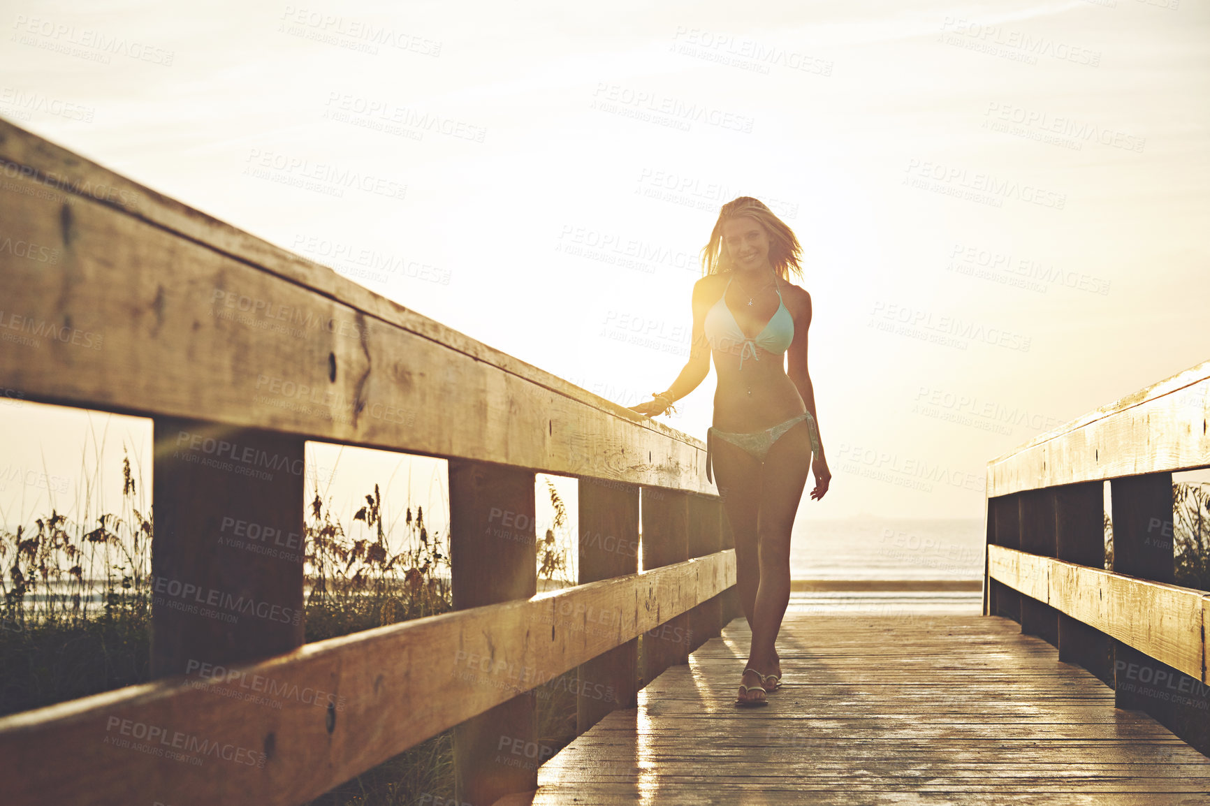 Buy stock photo Shot of a young woman in a bikini on a walkway near the beach