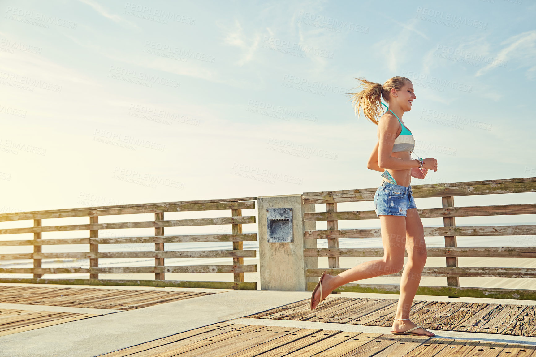 Buy stock photo Shot of a young woman in a bikini on a walkway near the beach