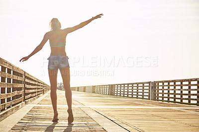 Buy stock photo Shot of a young woman in a bikini on a walkway near the beach
