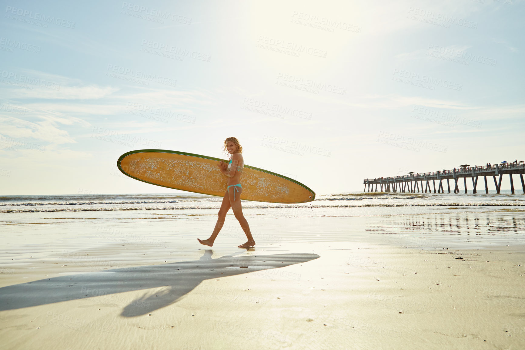 Buy stock photo Shot of an attractive young woman carrying her surfboard on the beach