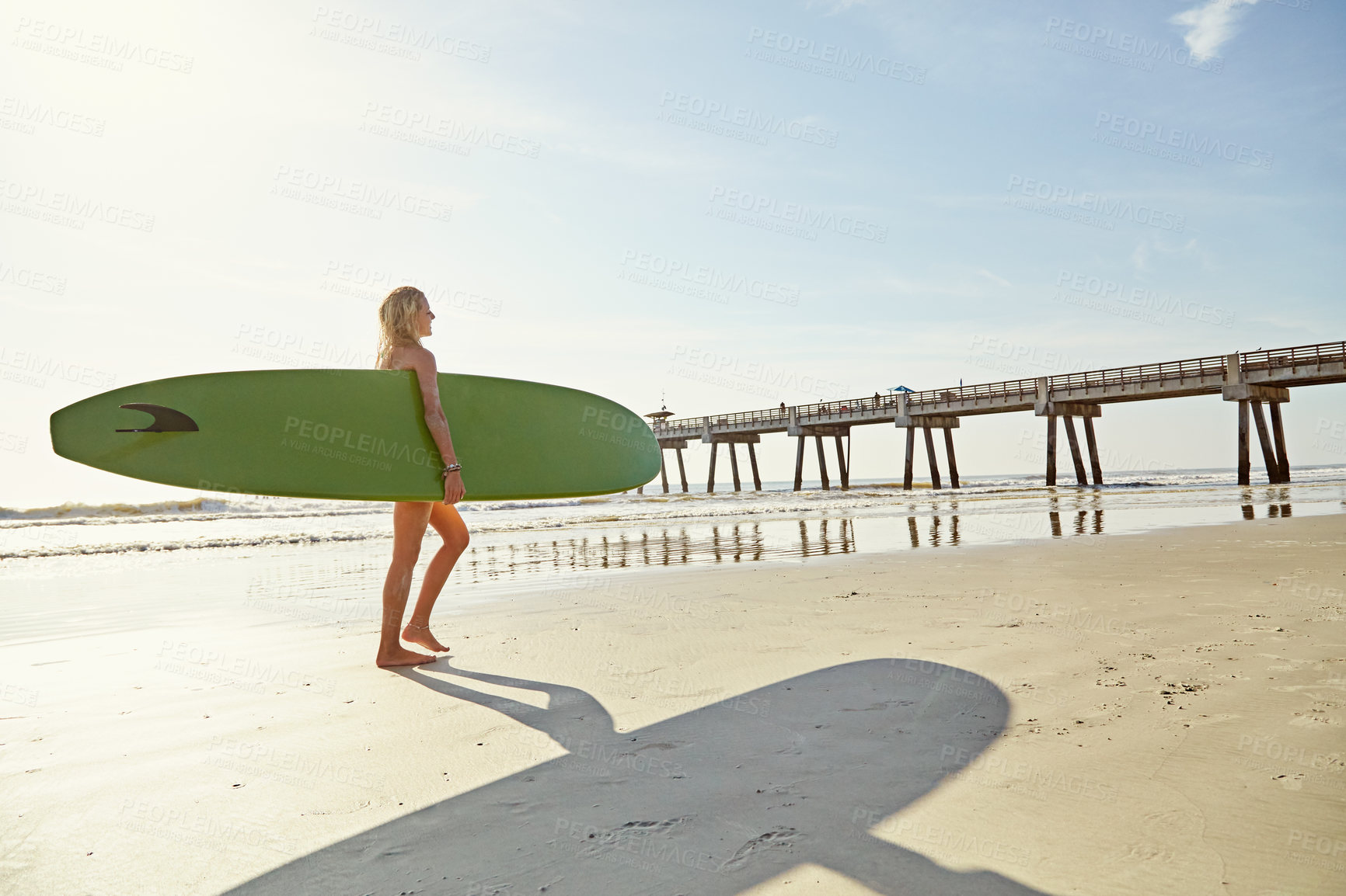 Buy stock photo Rearview
shot of an attractive young woman carrying her surfboard on the beach