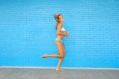 Buy stock photo Portrait of an attractive young woman running against a blue brick wall