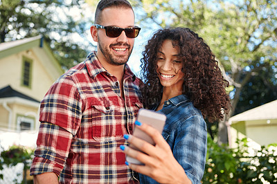 Buy stock photo Shot of a young couple standing outside looking at something on a cellphone