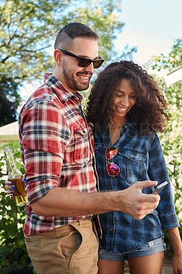 Buy stock photo Shot of a young couple standing outside looking at something on a cellphone