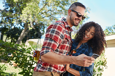 Buy stock photo Shot of a young couple standing outside looking at something on a cellphone
