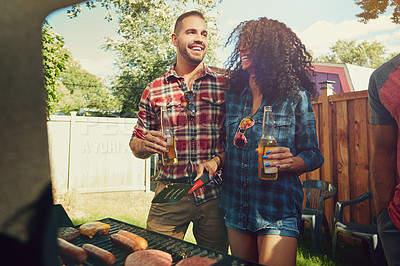 Buy stock photo Shot of a young couple standing by a barbecue grill outside