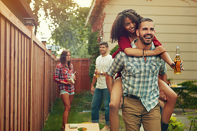 Buy stock photo Shot of a young man piggybacking his girlfriend with people standing in the background