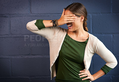 Buy stock photo Shot of a young woman covering her eyes against a brick wall background