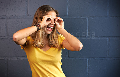 Buy stock photo Shot of a young woman looking through her fingers against a brick wall background