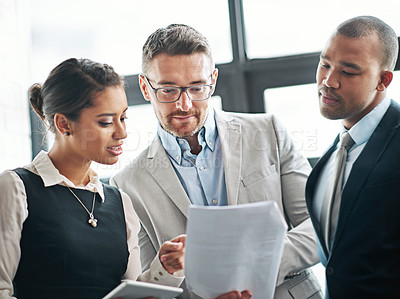 Buy stock photo Cropped shot of three businesspeople looking over some paperwork in the office