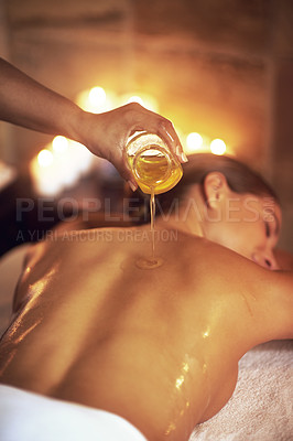 Buy stock photo Shot of a masseuse pouring oil on a woman's back before her massage