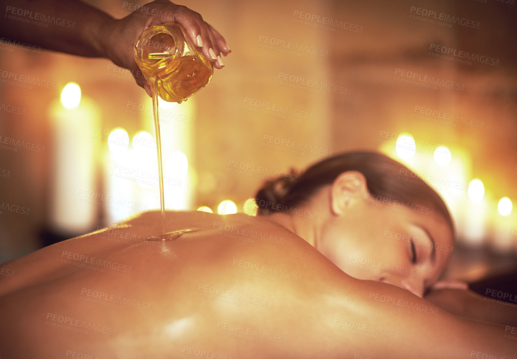 Buy stock photo Shot of a masseuse pouring oil on a woman's back before her massage