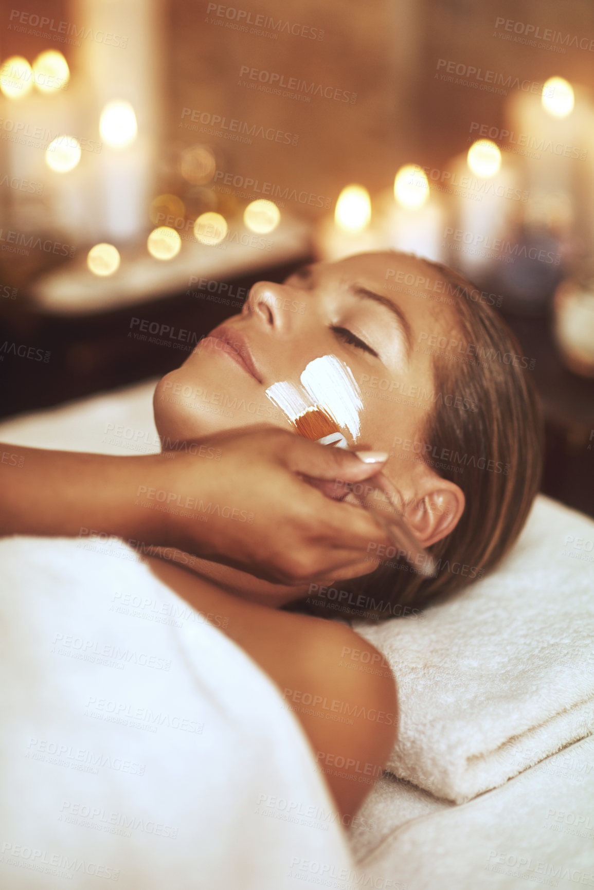 Buy stock photo Woman, facial and treatment with brush for spa holiday or skincare beautician, stress relief or dermatology. Female person, hand and face mask with candle bokeh at Bali resort, self care or hotel