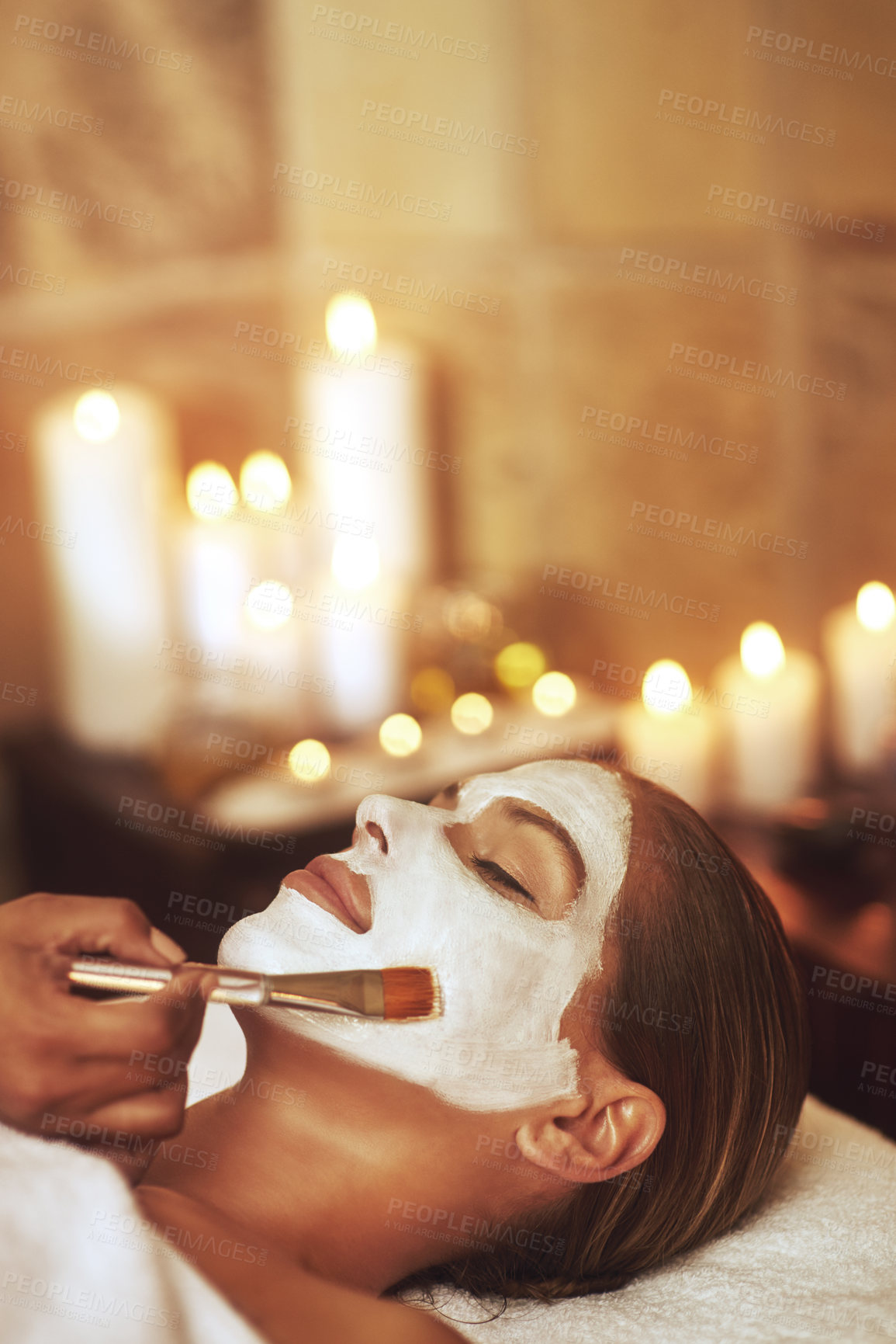 Buy stock photo Woman, face mask and hand brush in spa for holiday treatment or beautician, stress relief or dermatology. Female person, calm and facial with candle bokeh at Bali resort in hotel, relax or skincare